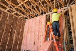 Contractor installing pink fiberglass batt insulation in an unfinished building.